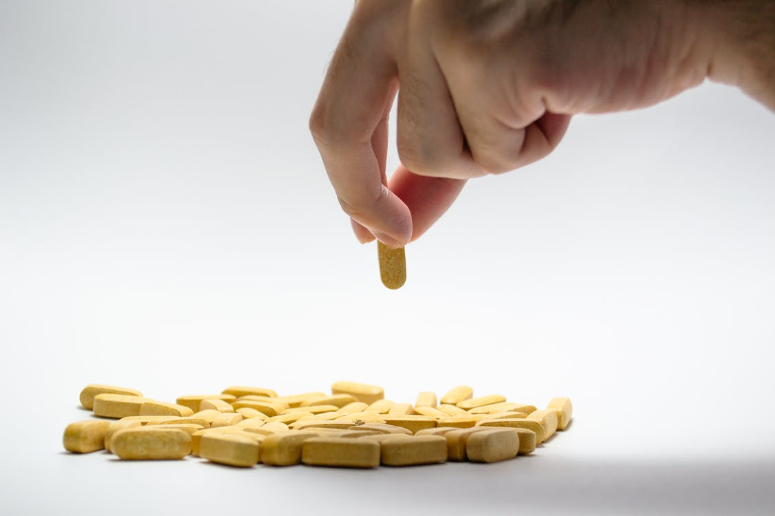 An image of a hand picking a yellow tablet from a pile of pills