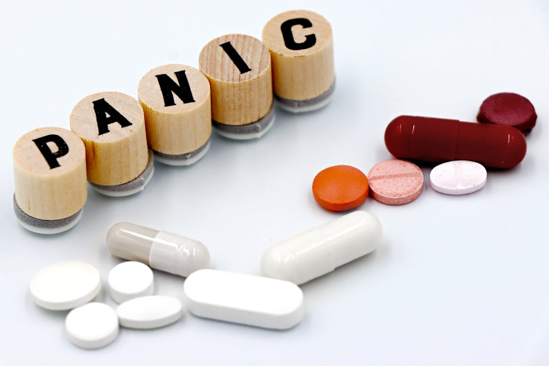 The word panic spelled on wooden tiles next to an assortment of pills 