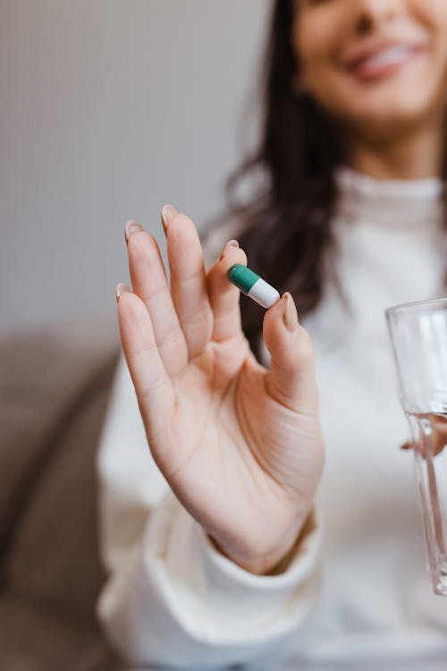 A person holding a capsule and a glass of water