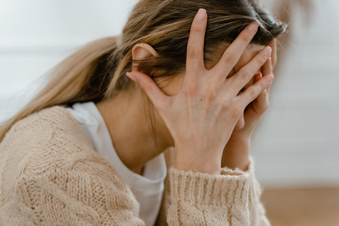A person sitting indoors with face covered by hands, expressing stress and frustration.